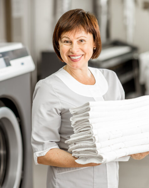 Senior washwoman in the laundry Portrait of a senior washwoman in uniform standing with towels in the hotel laundry