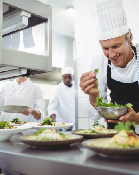 Happy chef garnishing appetizer plates at order station in restaurant